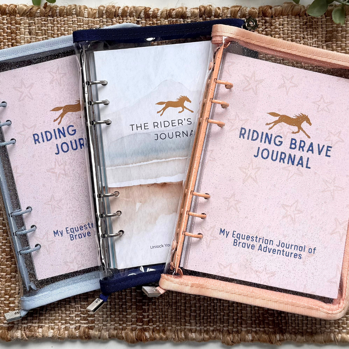 Two equestrian journals titled 'Riding Brave Journal' on a woven mat with greenery in the background.