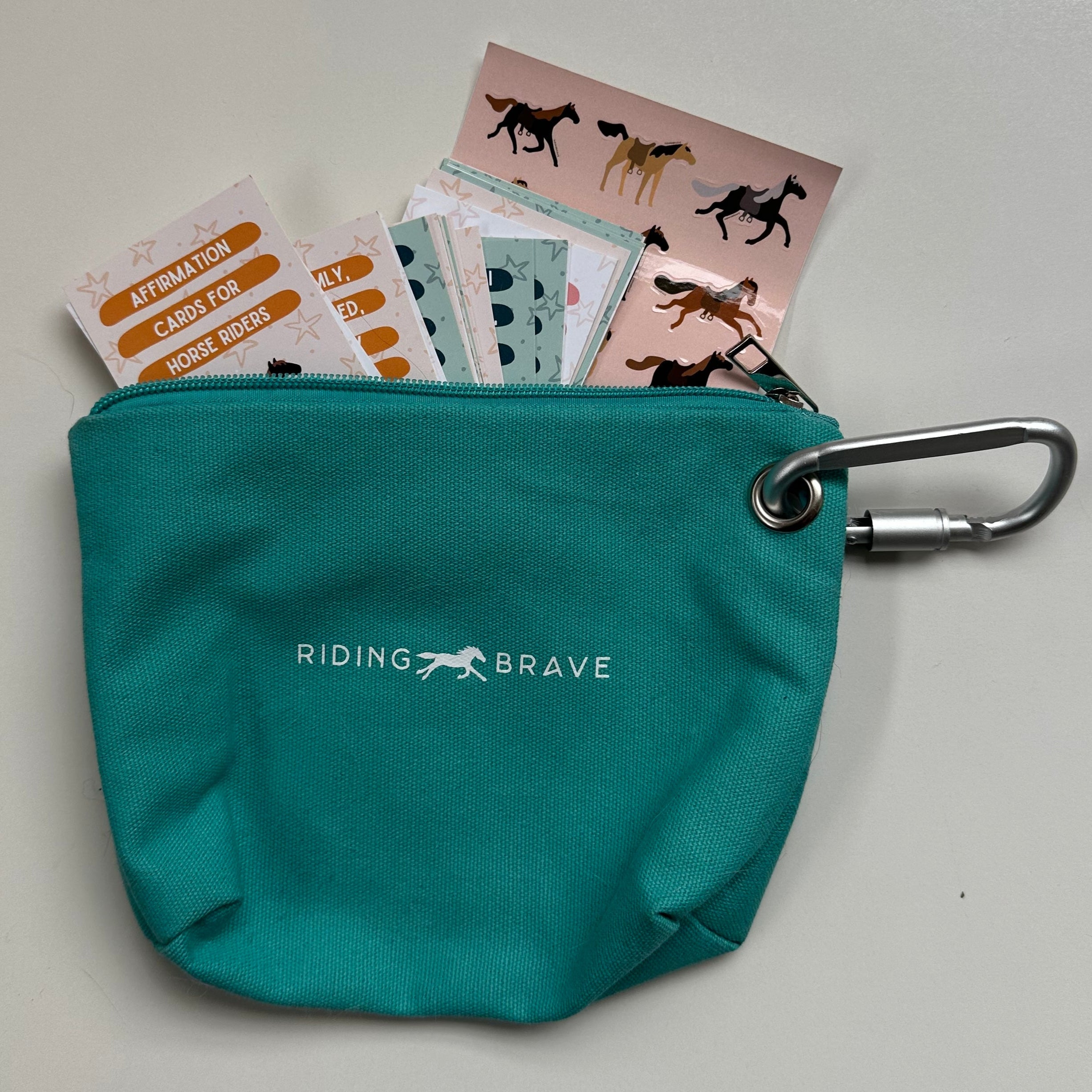 Teal pouch with 'Riding Brave' logo containing cards on a light gray background